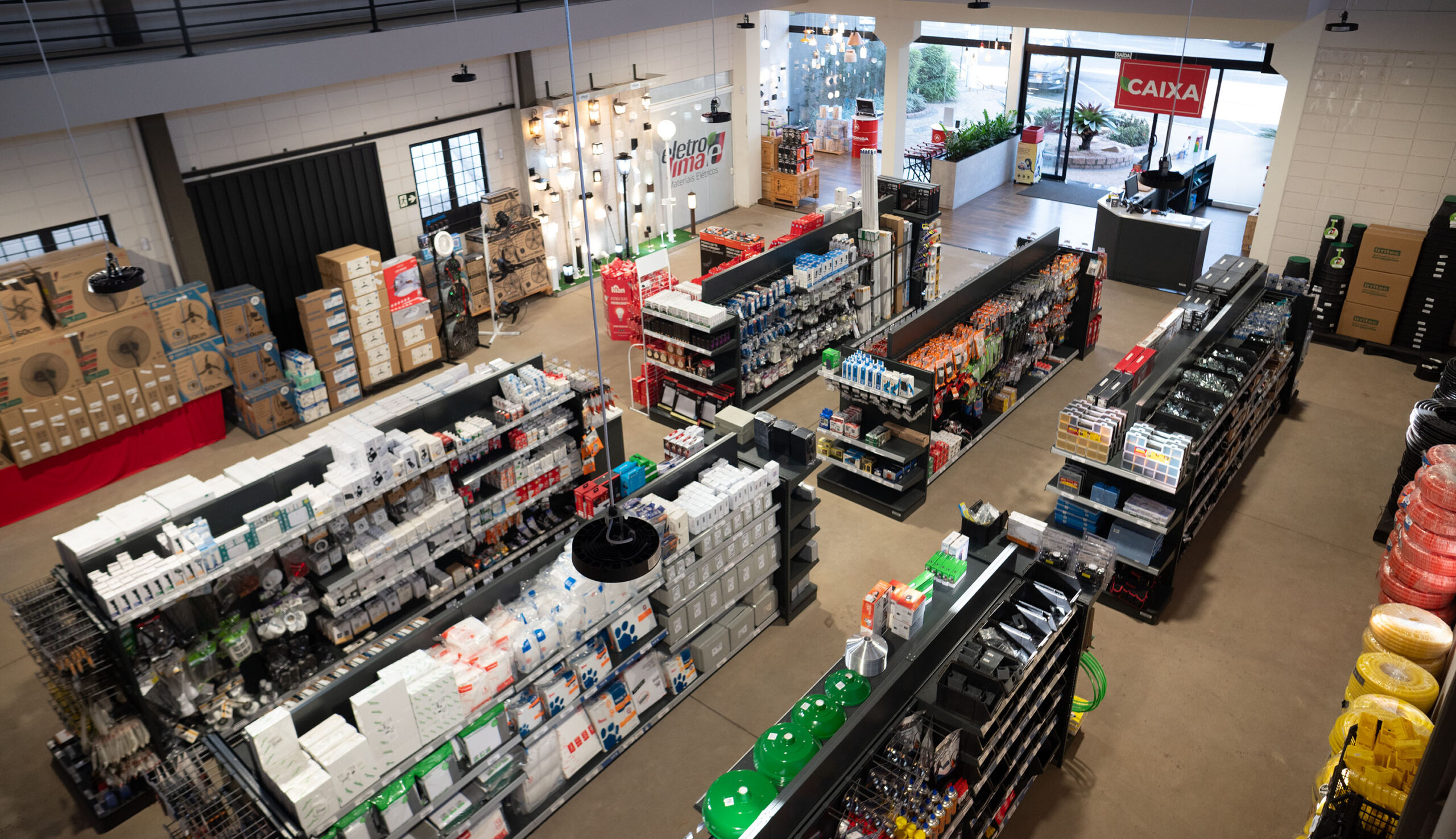 Vista aérea do interior da loja Eletrolima com prateleiras organizadas de materiais elétricos, produtos diversos, iluminação e balcão de atendimento ao fundo.